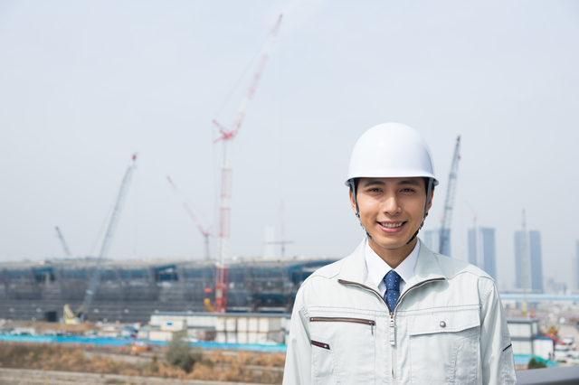 建設現場を背景に笑顔の男性技術職員
